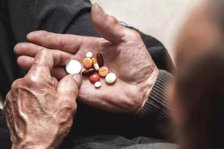 old man hands holding many pills of medication