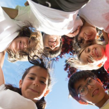 kids in a circle hugging and looking down with camera view from below and within the huddle