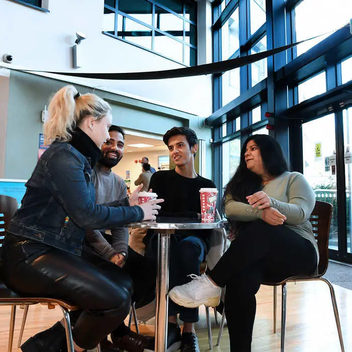 4 students sitting around a table drinking coffee.