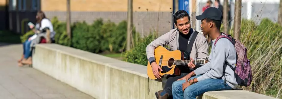 two student sitting one playing the guitar