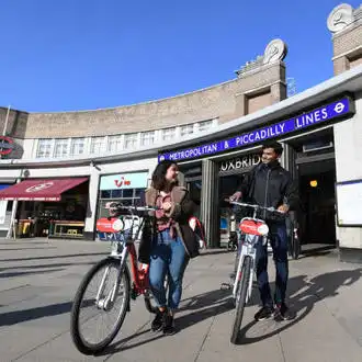 Two Brunel students walking with bikes outside Uxbridge tube station