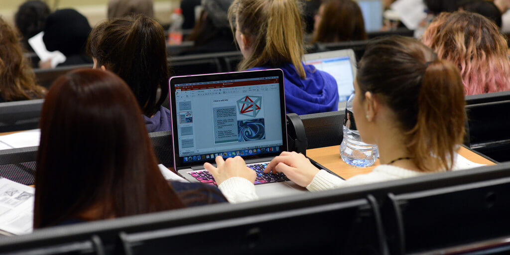 female student making notes on her laptop during lecture