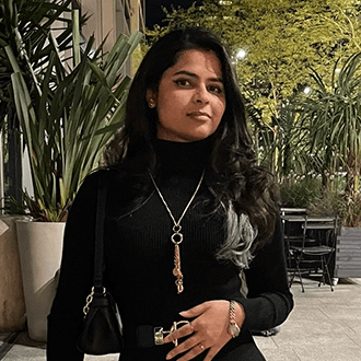 Female in a black outfit with a necklace, holding a purse, standing outdoors at night.