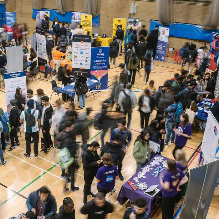 Busy indoor career fair with numerous attendees and exhibitors engaging at various booths