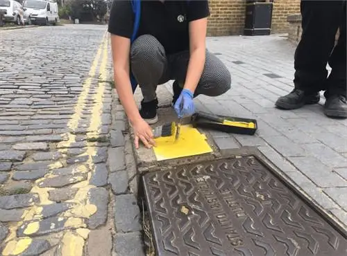 Environment agency worker stencilling a fish on the pavement as part of the yellow fish campaign