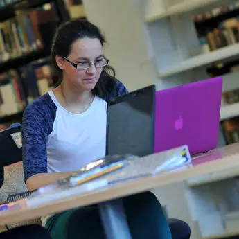 young female student working on a laptop in the library of Brunel University London