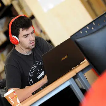 male students with headset working on a laptop in the library of Brunel University London