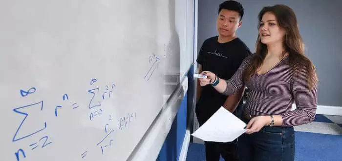 Two students writing maths equation on a white board