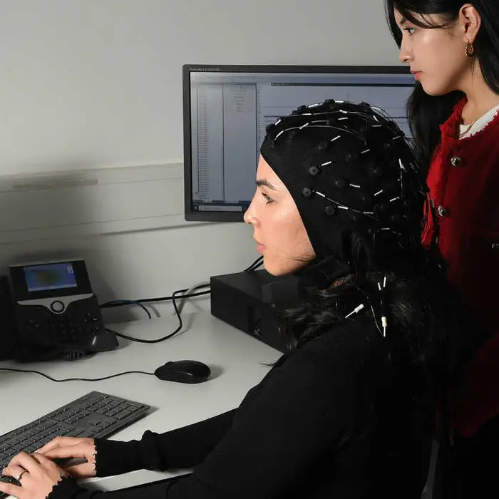 two female students sitting at a computer and one student is wearing brain wave scanning equipment