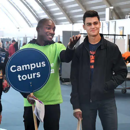 current student showing a prospective student around brunel, he is holding a campus tour sign.