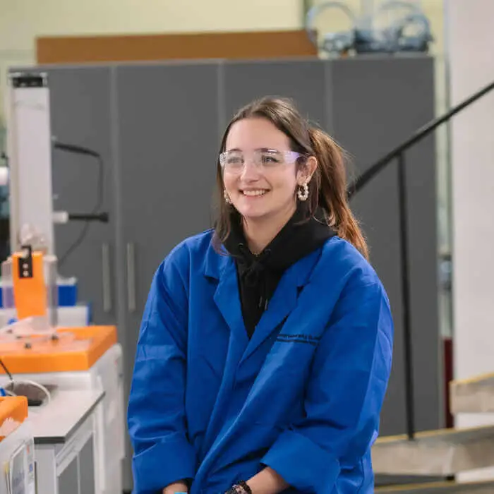 Person in blue lab coat sitting in a laboratory setting