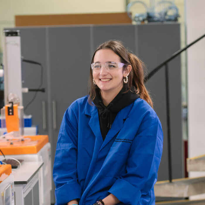 Person in blue lab coat sitting in a laboratory setting