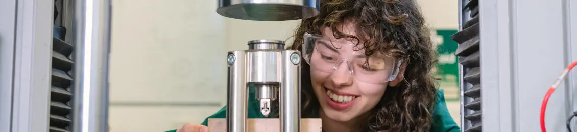 Student in lab coat operating a mechanical testing machine