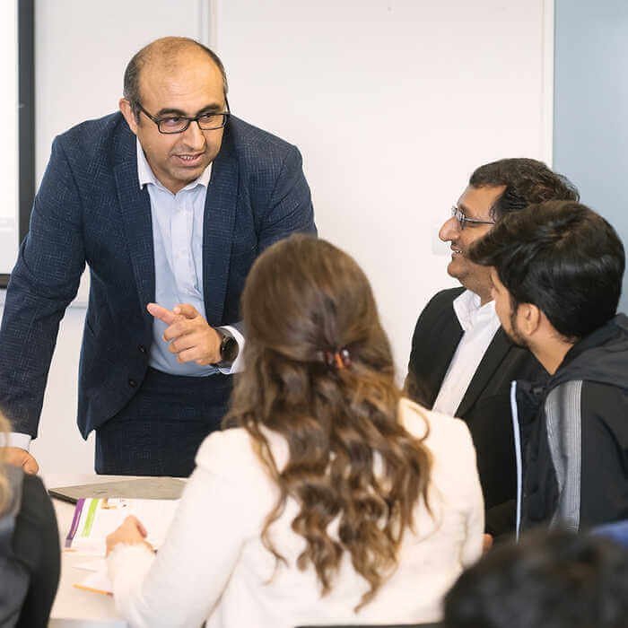A group of people engaged in a meeting, with one person presenting and others attentively listening around a table