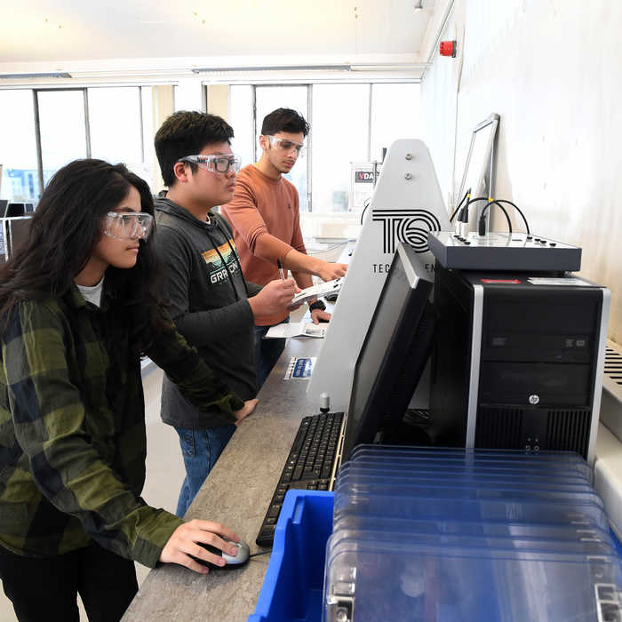 Two male and one female student using technical equipment in an engineering lab
