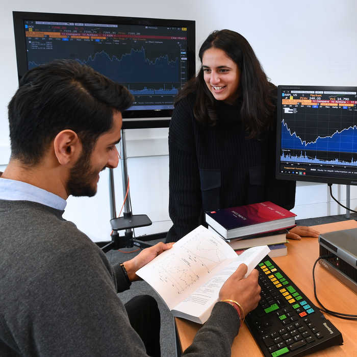 Male and female student talking and looking at the finance book