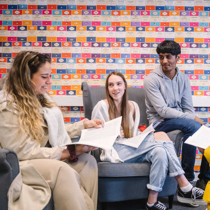 A female student reading a book and talking to two other students